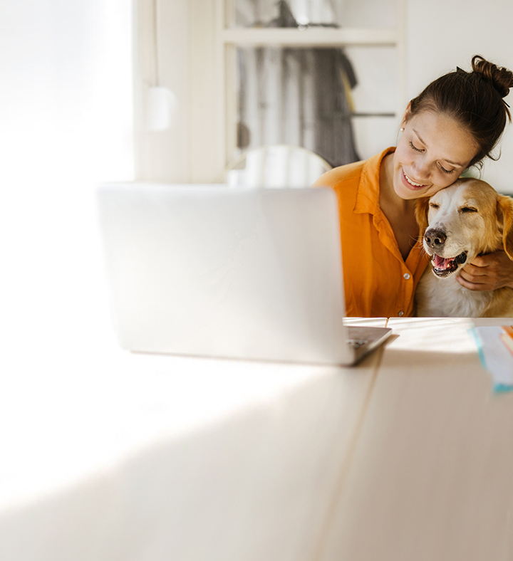 Frau kuschelt mit Hund vor Schreibtisch.
