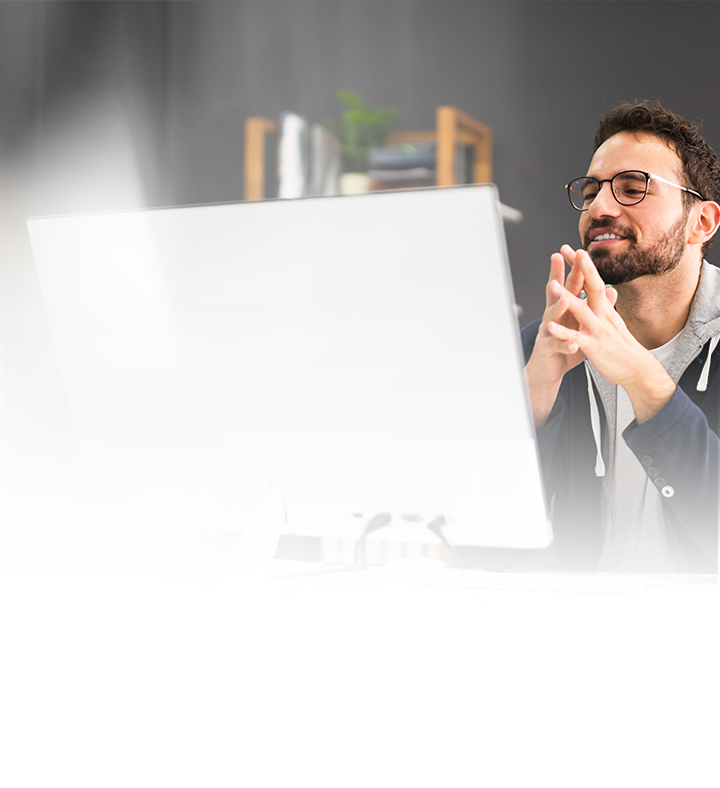 Mann vor PC-Monitor faltet glücklich die Hände zusammen.